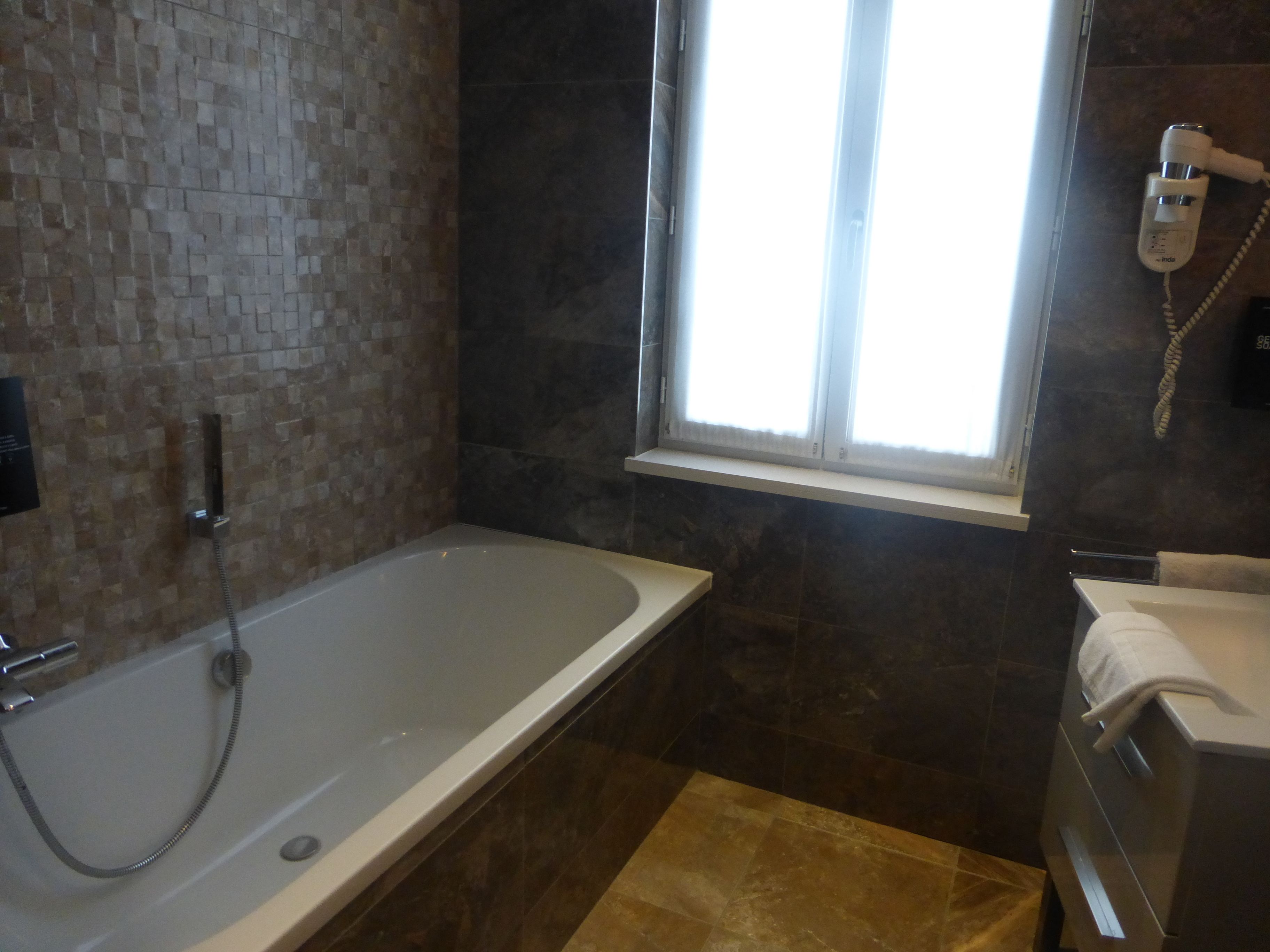 A bathroom with a bathtub, a window, a towel rack, and a shower.