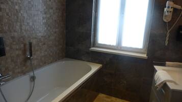 A bathroom with a bathtub, a window, a towel rack, and a shower.