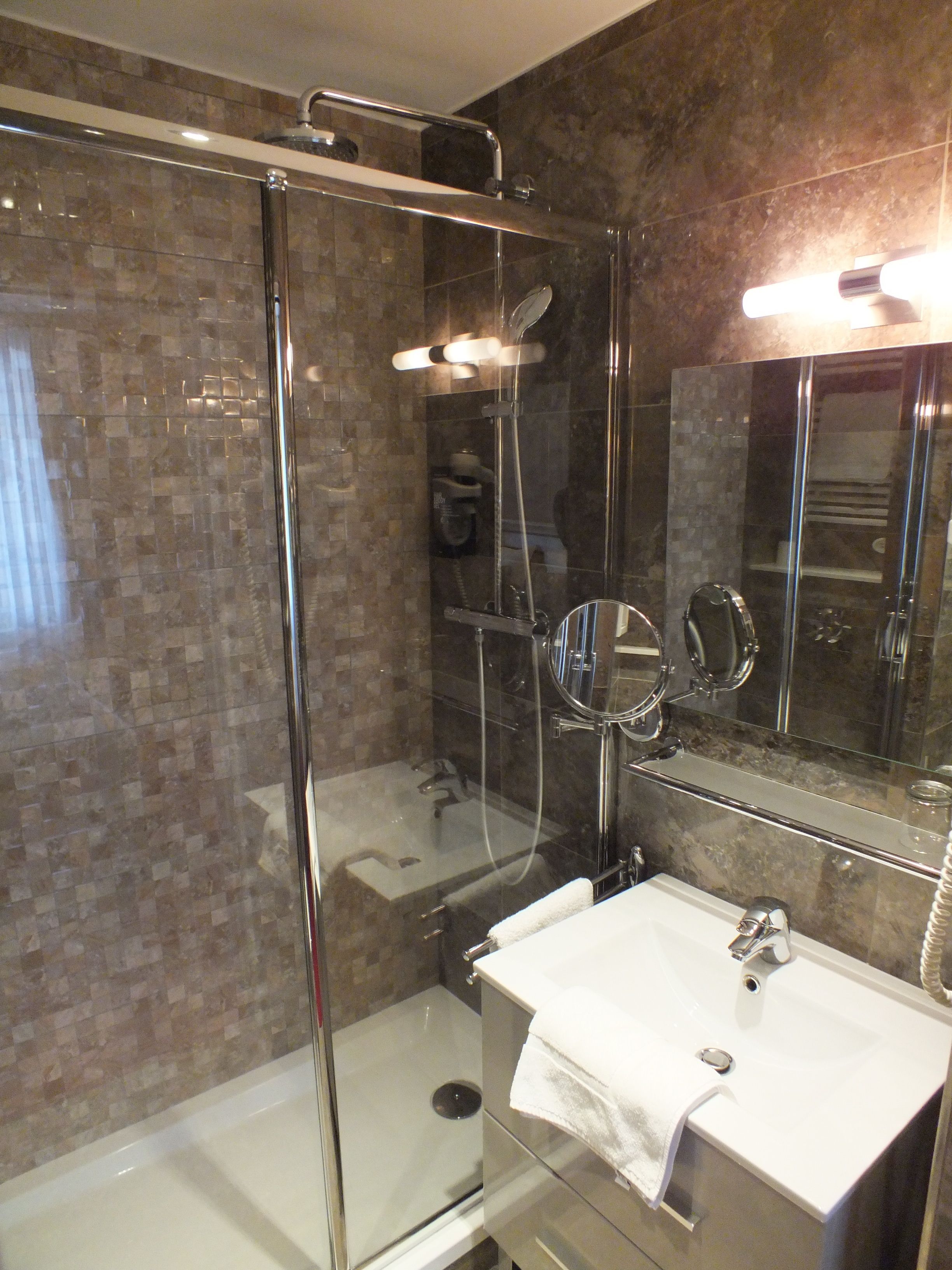 A modern bathroom with a glass-enclosed shower, a white sink, and a large mirror.