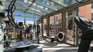 Un gimnasio al aire libre con equipo de ejercicio, un cerramiento de vidrio y vistas a la ciudad.