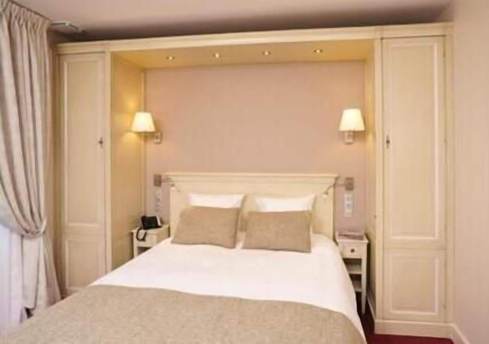 Una habitación de hotel con una cama grande, dos lámparas de noche, una mesita de noche y un armario.