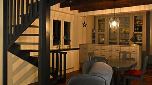 Un espace repas avec un escalier en bois, un lustre et une cuisine en arrière-plan.