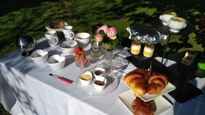 Une table dressée avec des tasses et des soucoupes blanches, un cloche en verre, des croissants et divers condiments.