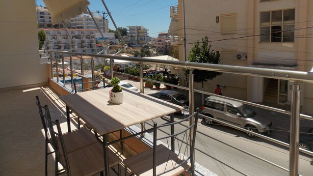 A balcony with a wooden table and chairs, overlooking a street with cars and buildings. - Amber Apartments (Sarandë)