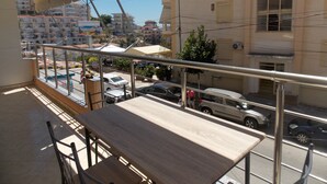 A balcony with a view of a city street, a table, and chairs. - Amber Apartments (Sarandë)