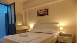 A hotel room with a large bed, two bedside tables with lamps, a painting on the wall, and a door to a balcony. - Amber Apartments (Sarandë)