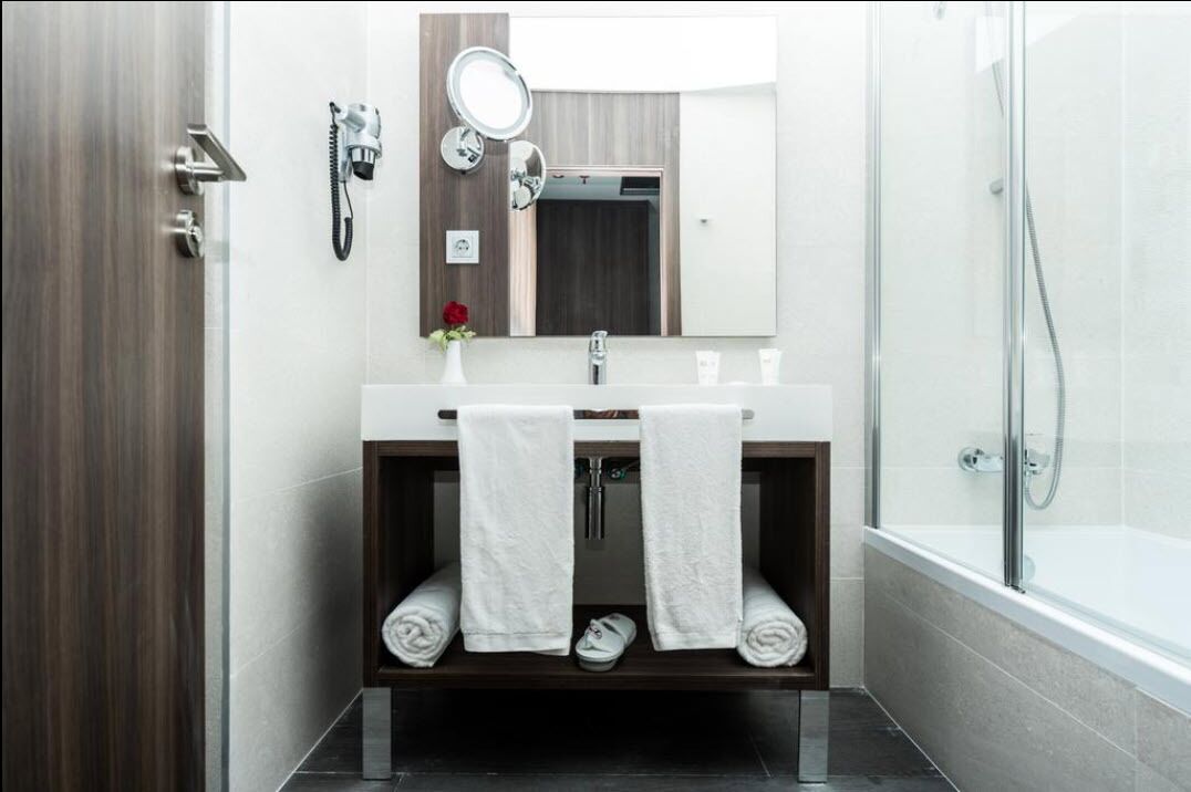 Un baño moderno con tocador de madera, un espejo, ducha y toallero.