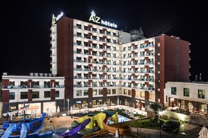 Un hotel de varios pisos con balcones, una zona de piscina con toboganes y mobiliario exterior.