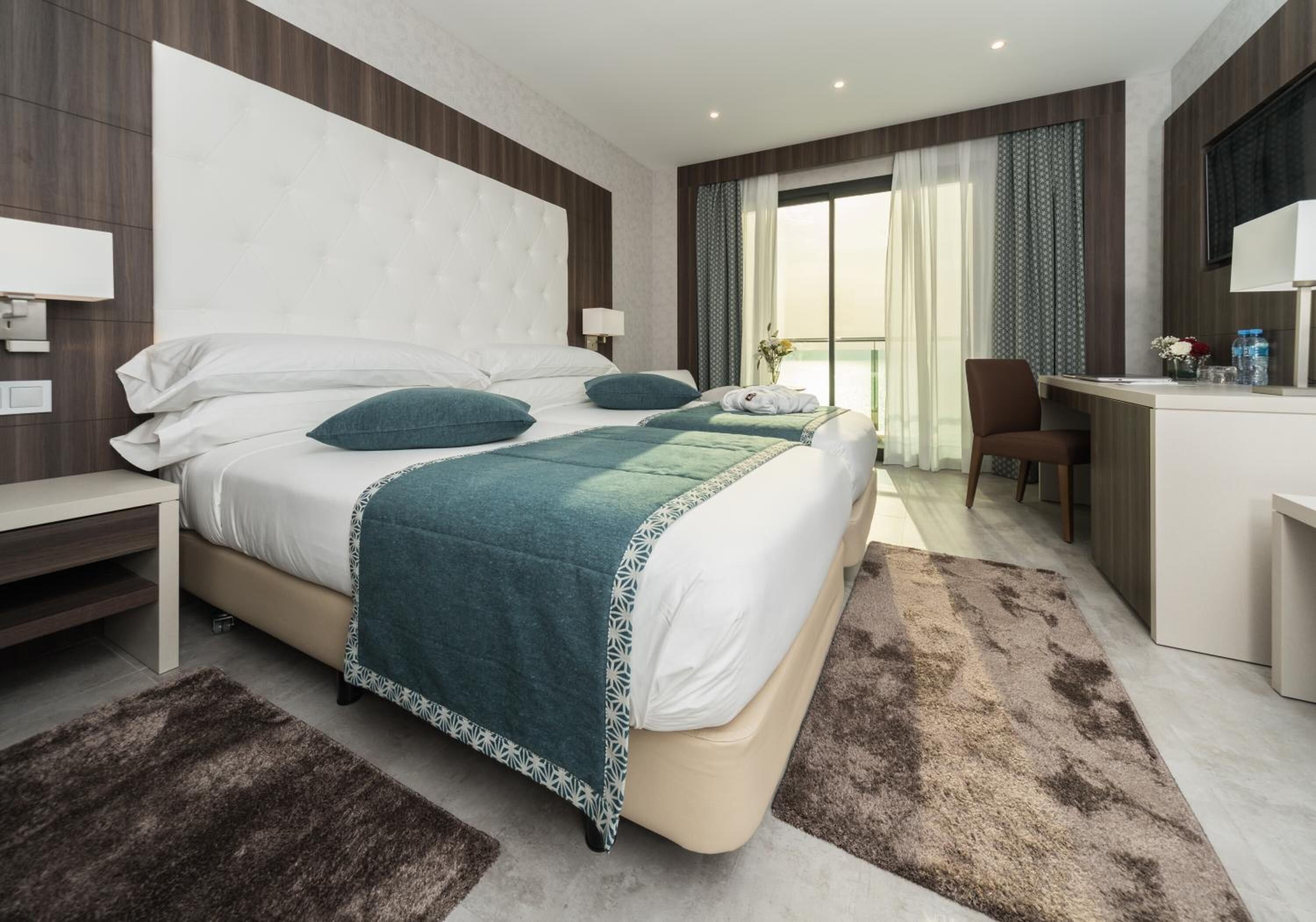 Quarto de hotel moderno com uma cama grande, uma escrivaninha e vista para o exterior.