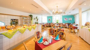 A dining area with multiple tables and chairs, a buffet counter with food and drinks, and a kitchen area in the background. - Hotel St. Martin (Marktoberdorf)