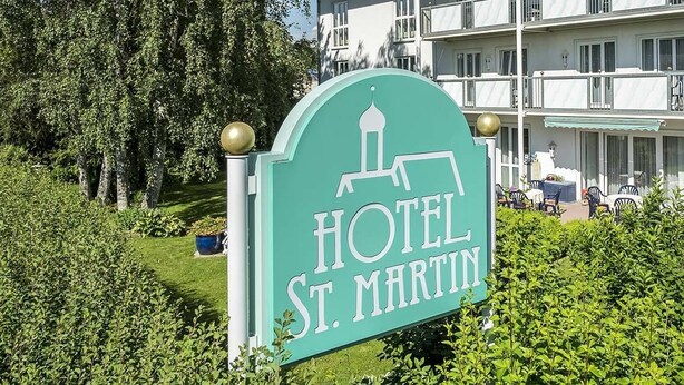 A sign for Hotel St. Martin with a clear view of the building's exterior, including balconies and outdoor seating. - Hotel St. Martin (Marktoberdorf)