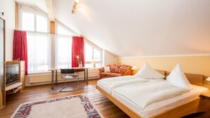 A bedroom with a bed, a desk, a chair, a TV, and a window with curtains. - Hotel St. Martin (Marktoberdorf)