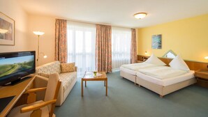 A hotel room with a sofa, two single beds, a TV, a desk, and a lamp. - Hotel St. Martin (Marktoberdorf)
