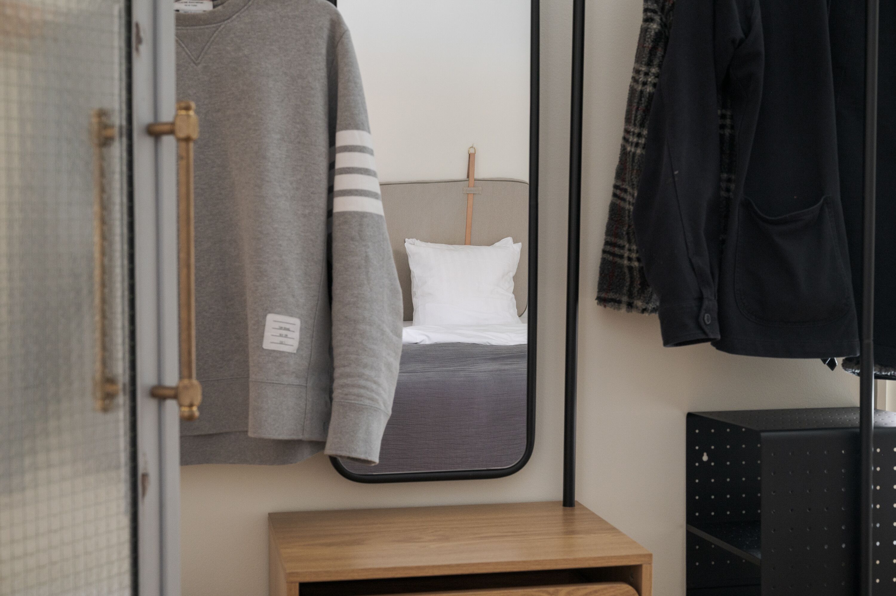 A bedroom with a bed, a mirror, a wooden nightstand, and a hanging coat rack.
