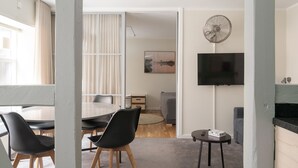 A modern living room with a dining area, a flat-screen TV mounted on the wall, and a ceiling fan. - The Brewer apartments by Daniel&Jacob’s (Copenhagen)