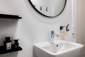 A bathroom with a white sink, a round mirror, and a black shelf with two bottles of hand soap. - The Brewer apartments by Daniel&Jacob’s (Copenhagen)