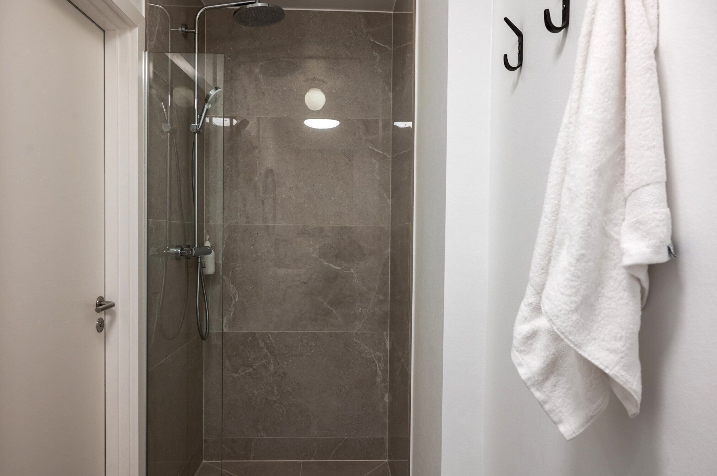 A modern bathroom with a glass-enclosed shower, a white towel hanging on the wall, and a marble floor.