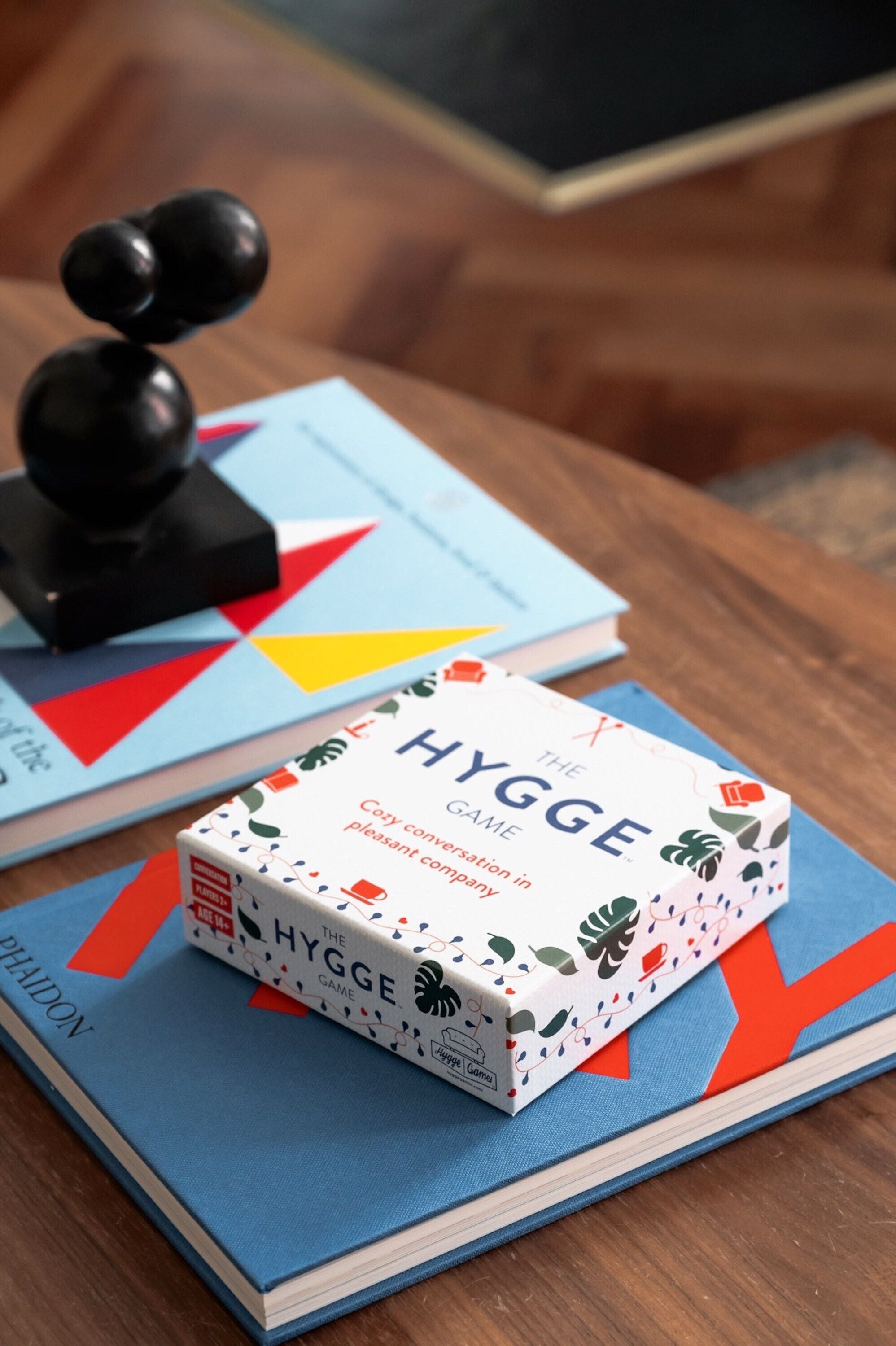 Ein Buch mit dem Titel 'The Hygge Game' auf einem Holztisch.
