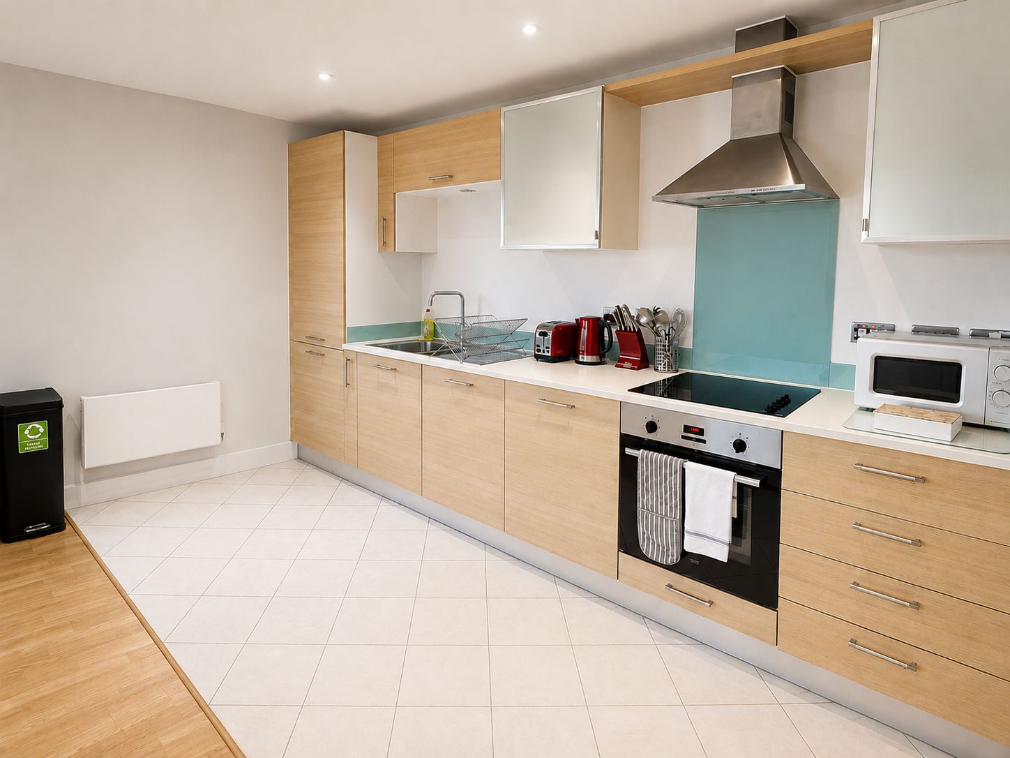 A modern kitchen with wooden cabinets, a built-in oven, a microwave, and a sink.