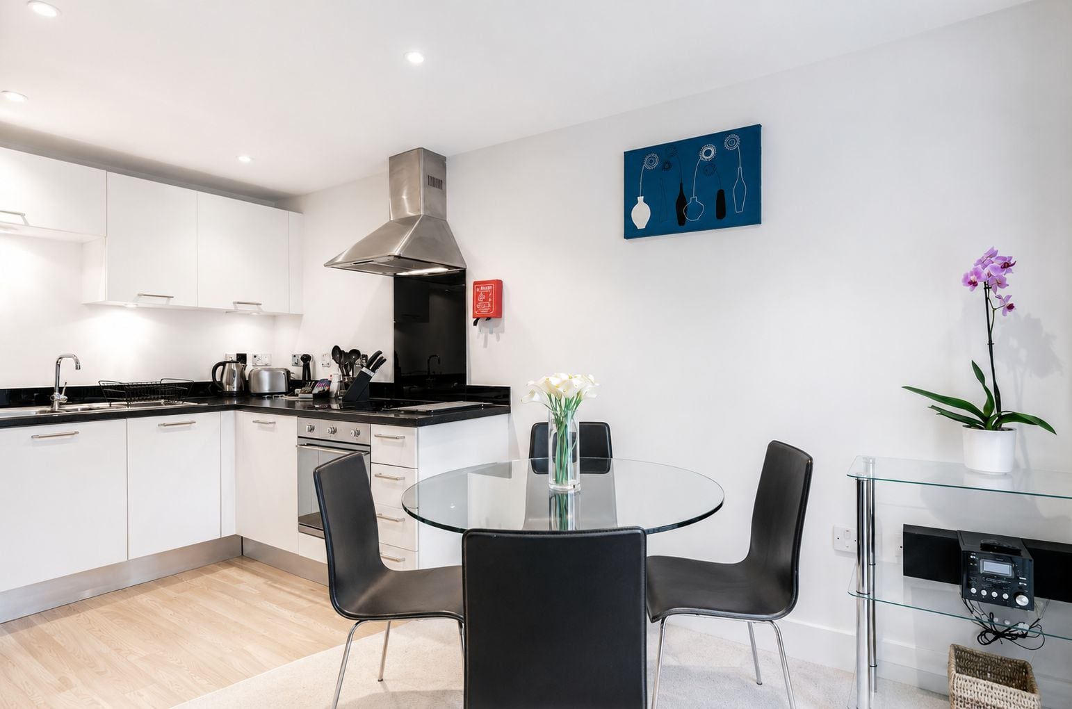 Une cuisine moderne avec des armoires blanches, une hotte de cuisinière en acier inoxydable et une table ronde en verre, accompagnée de deux chaises.