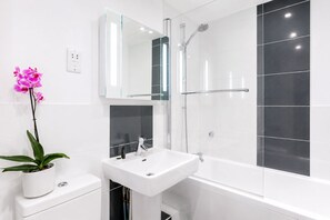 A modern bathroom with a white sink, a glass shower enclosure, and a potted orchid.