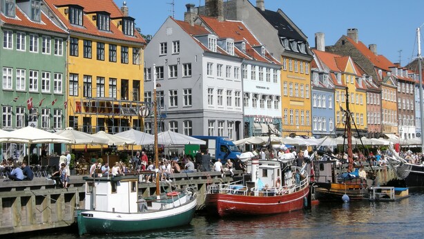 A waterfront area with colorful buildings, a dock with boats, and people enjoying the view.