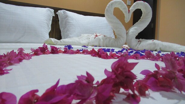 A bed with white linens, two swan-shaped towels, and pink and blue flower petals. - Kalamatiya Bird Sanctuary (Kalametiya)