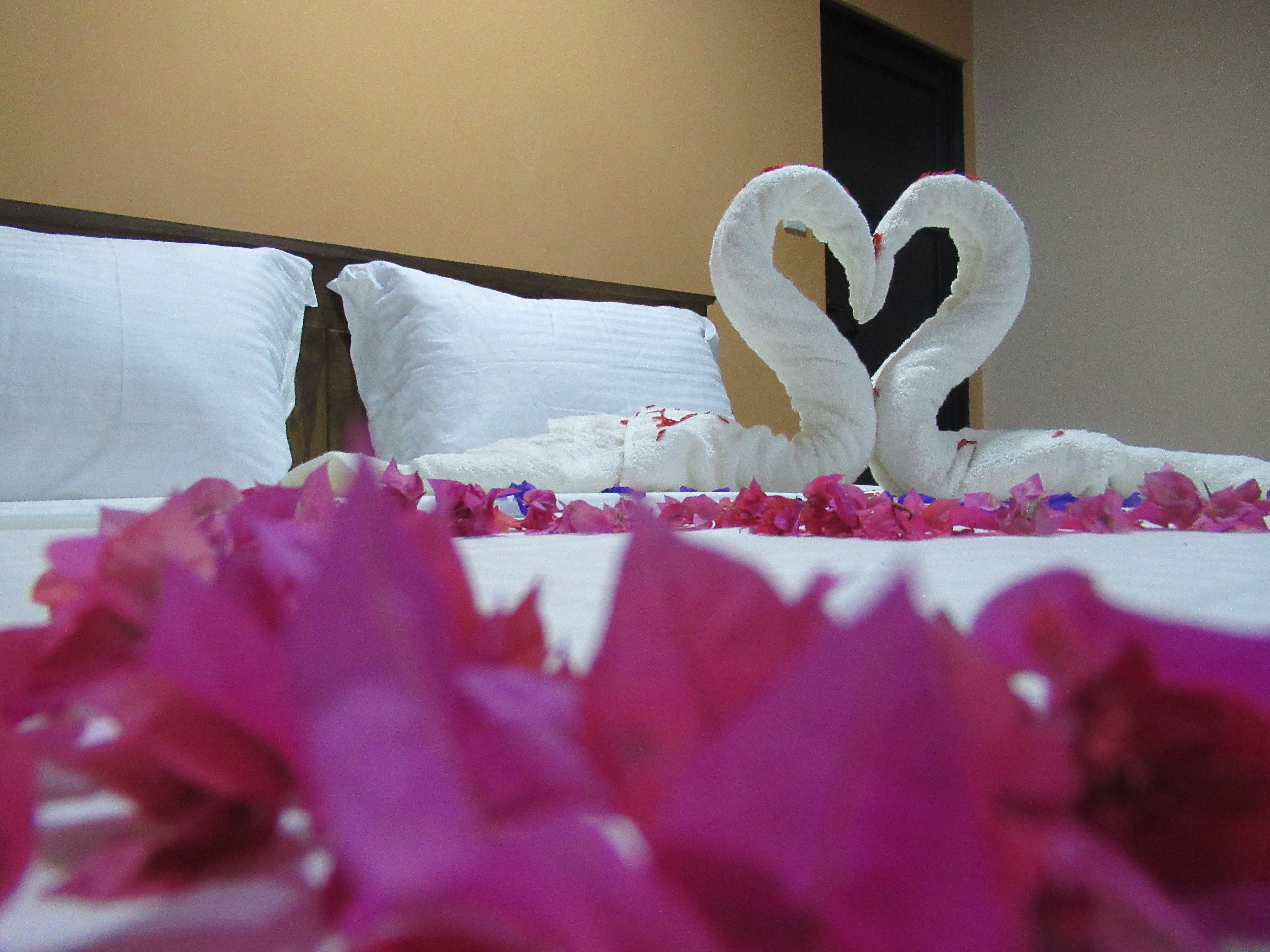 A bed with white linens and a heart-shaped towel arrangement on the pillows.