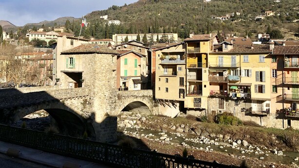 A stone bridge over a river with buildings on either side, including a multi-story structure with balconies. - Hostellerie du Pont Vieux (Sospel)