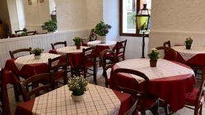 A restaurant with round tables covered in red and white checkered tablecloths, wooden chairs, and potted plants. - Hostellerie du Pont Vieux (Sospel)