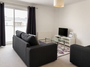 A modern living room with a sofa, a glass coffee table, a flat-screen TV, and a white cabinet. - Roomspace Apartments -Cascades Court (London)