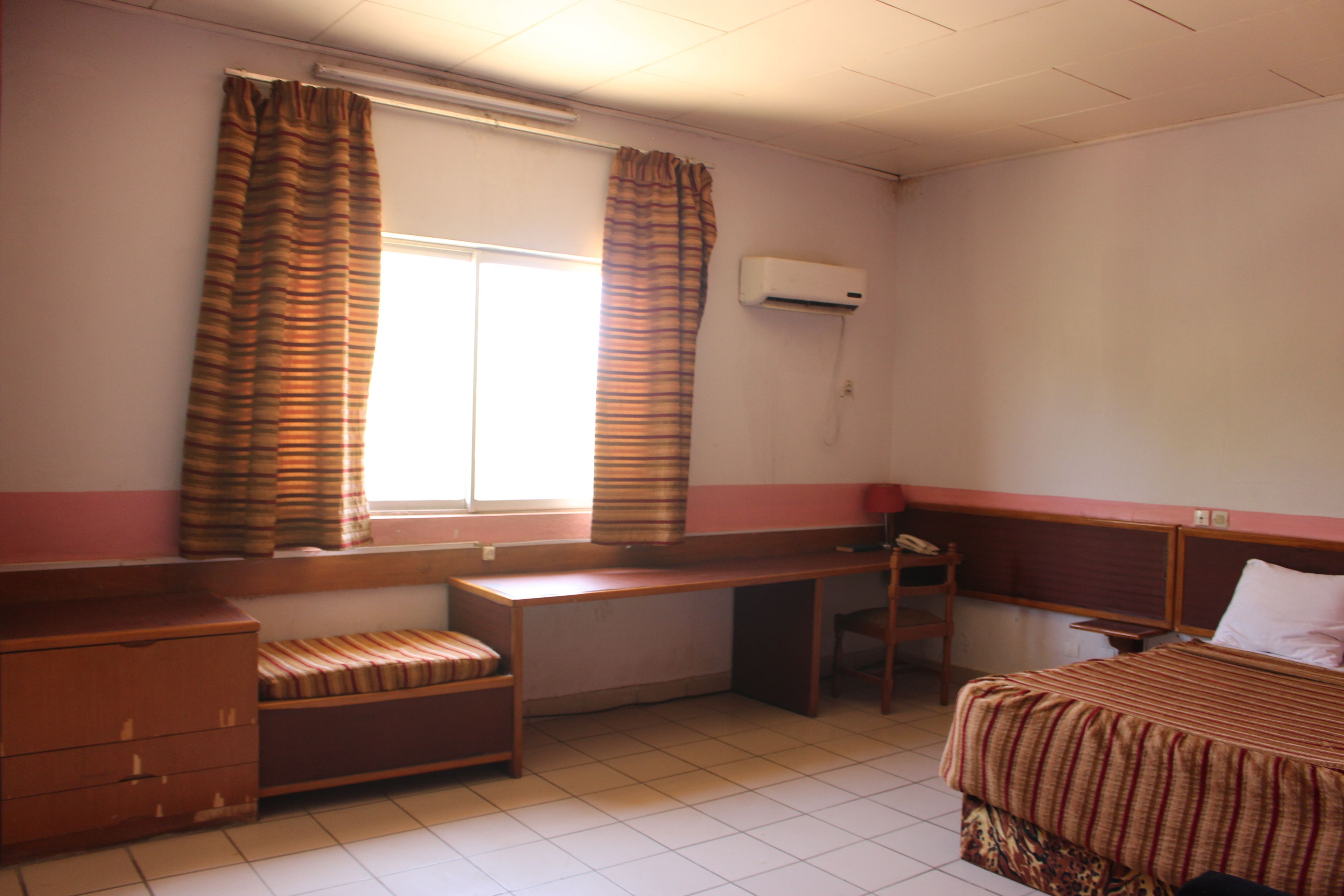A hotel room with a bed, a desk, a chair, a wardrobe, and a window with curtains.