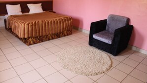 A bedroom with a bed, a chair, and a rug. - Hotel Maroua Palace (Maroua)