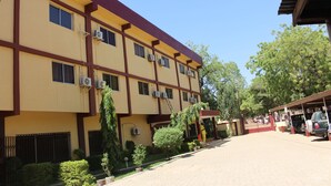A multi-story building with air conditioning units, a covered parking area, and a red fence. - Hotel Maroua Palace (Maroua)