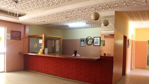 A reception area with a red counter, a clock, and framed pictures on the wall. - Hotel Maroua Palace (Maroua)