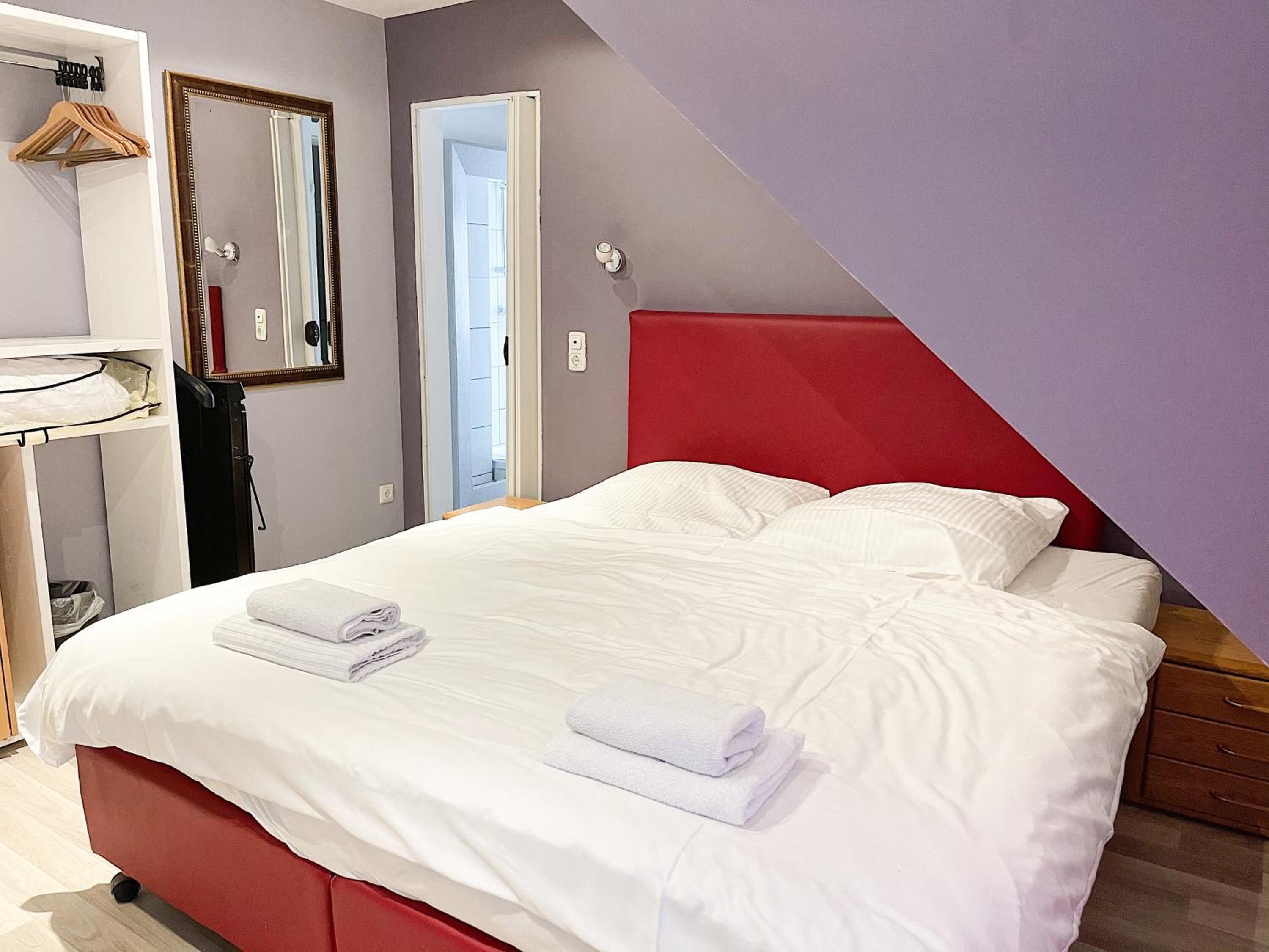 Un dormitorio con cabecera roja, ropa de cama blanca y dos toallas sobre la cama.