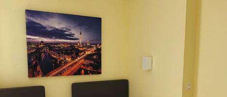 Una habitación de hotel con dos camas individuales, un cuadro de paisaje urbano en la pared y una pared amarilla lisa.