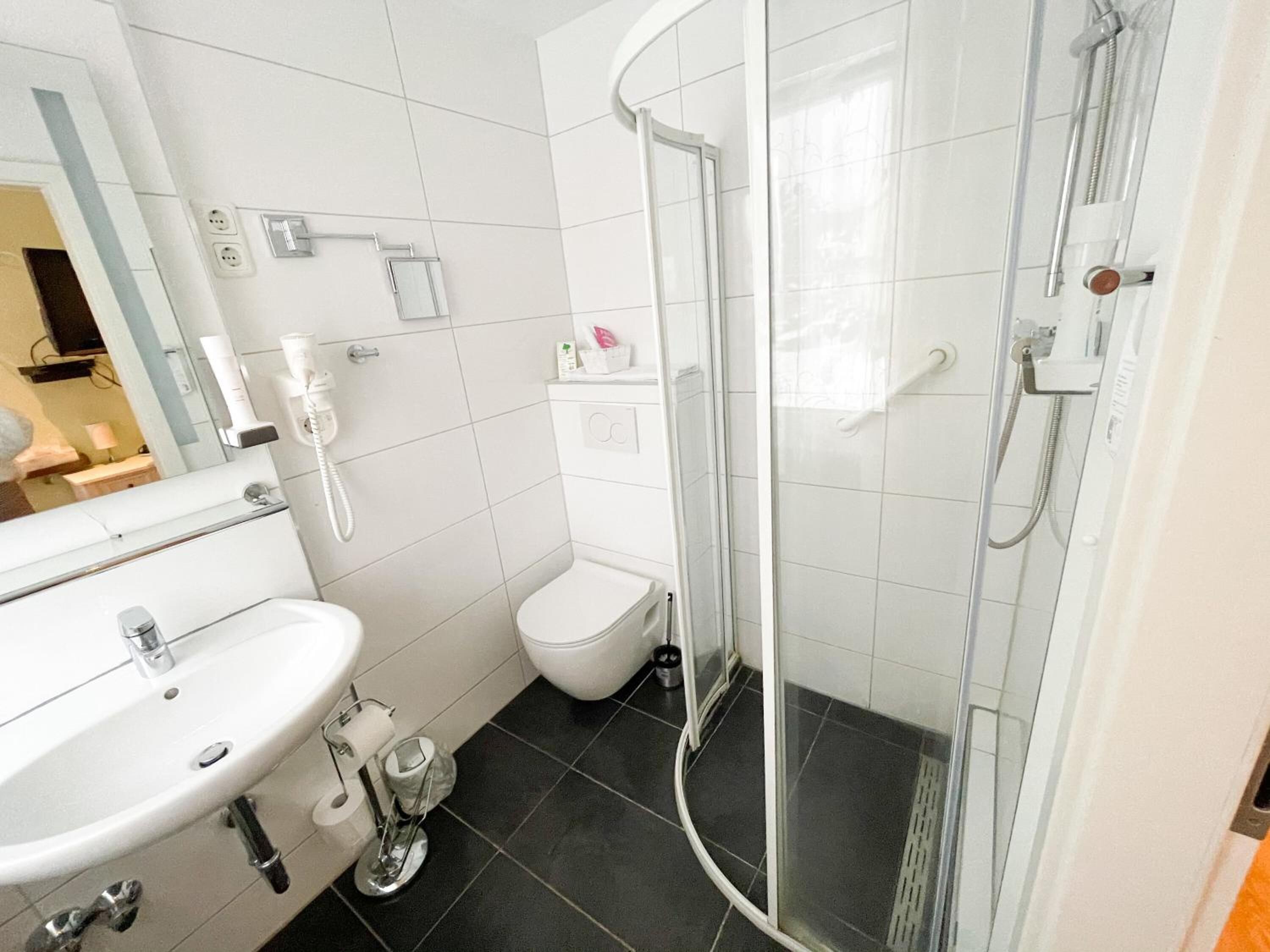 Un baño moderno con lavabo blanco, inodoro y ducha con mampara de vidrio.
