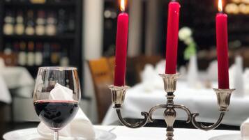 Una mesa dispuesta para cenar con una copa de vino, un candelabro con velas rojas y una rosa.