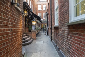 A narrow brick alley with steps leading to a building entrance, outdoor seating, and traditional street lamps. - Roomspace Apartments -Groveland Court (London)
