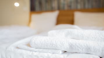 A neatly made bed with white linens and a folded white towel.