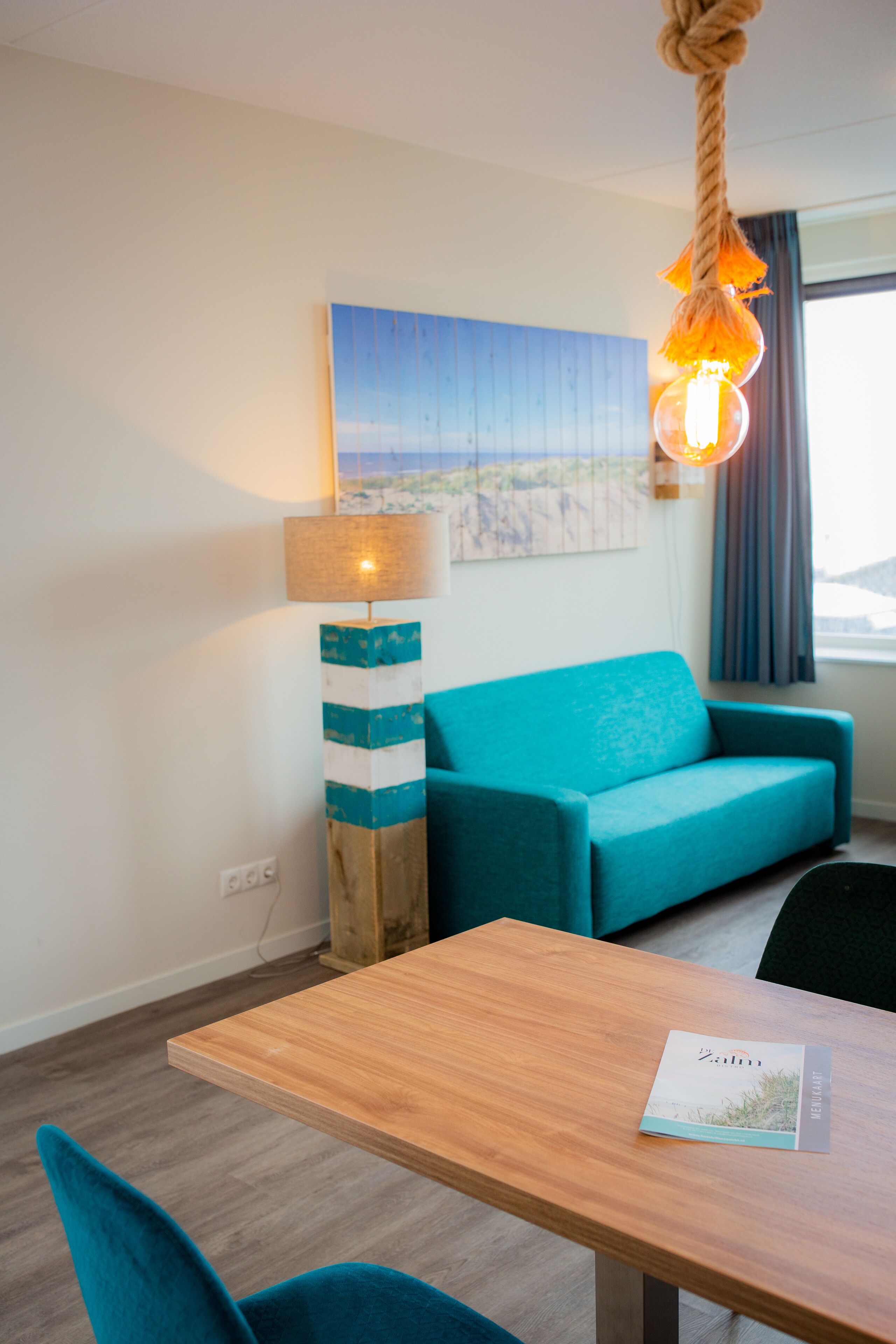 A modern room with a wooden table, teal sofa, and a lamp with a rope light.
