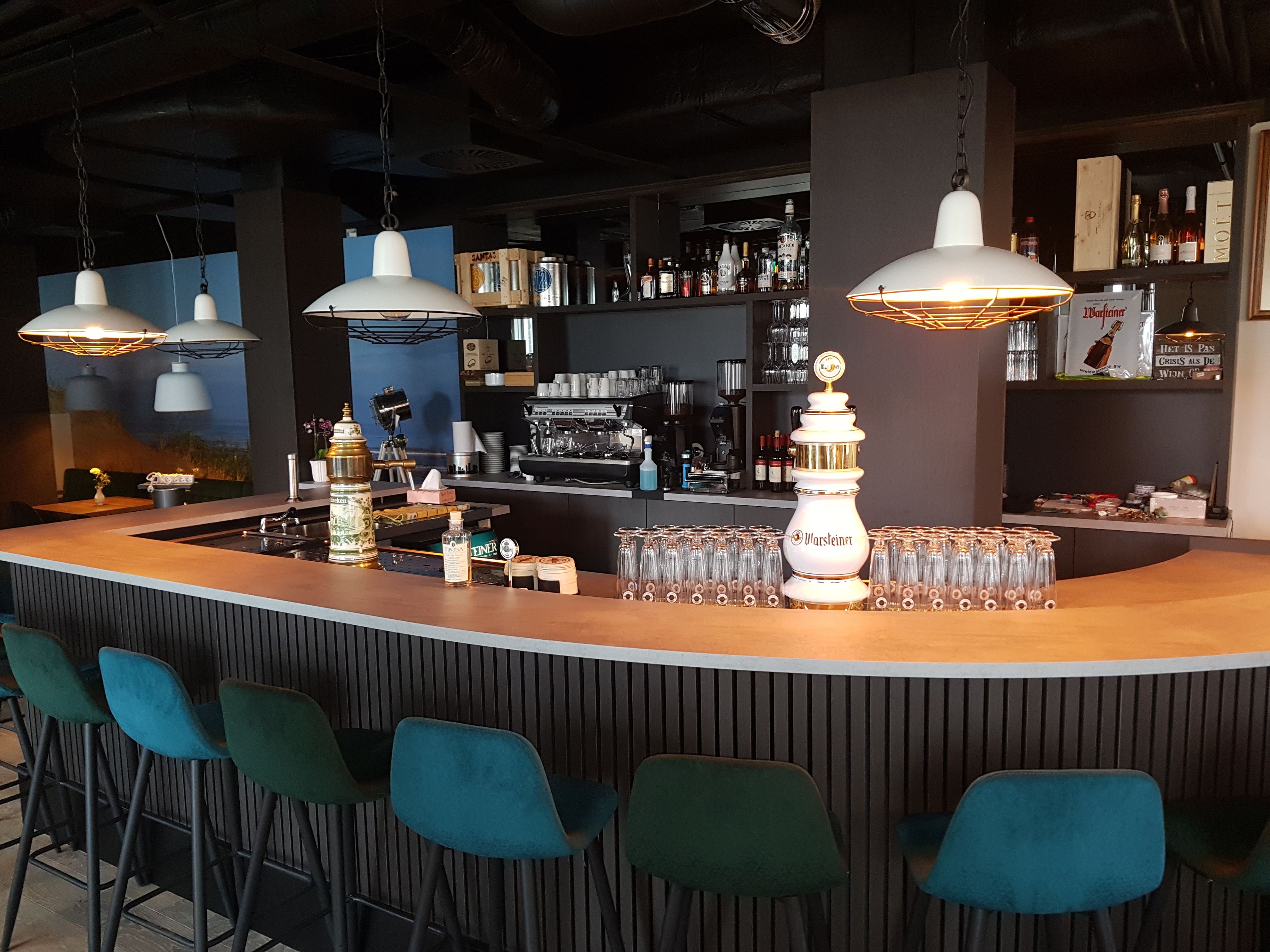 A bar area with a curved counter, multiple hanging pendant lights, and a selection of bar tools and glasses.