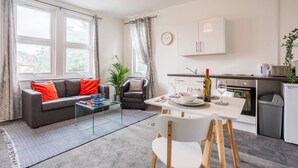 Ein modernes Wohnzimmer mit einer Couch, einem Couchtisch und einem Essbereich. Es gibt eine Küche mit Schränken, einer Spüle und einem Herd.