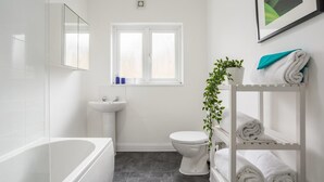 Ein modernes Badezimmer mit Badewanne, Toilette, Waschbecken und einem Fenster.