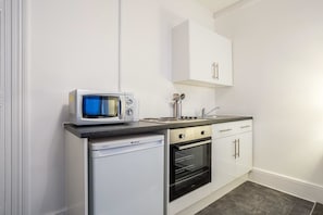 A compact kitchen with a microwave, dishwasher, oven, and white cabinets.