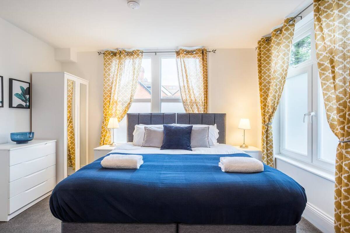 Een keurig opgemaakt slaapkamer met een groot bed, nachtkastjes, een kaptafel en gordijnen.