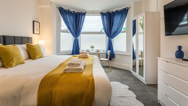Ein Hotelzimmer mit einem großen Bett, einem Schreibtisch, einem Sessel, einem Fernseher und einem Fenster mit Vorhängen.