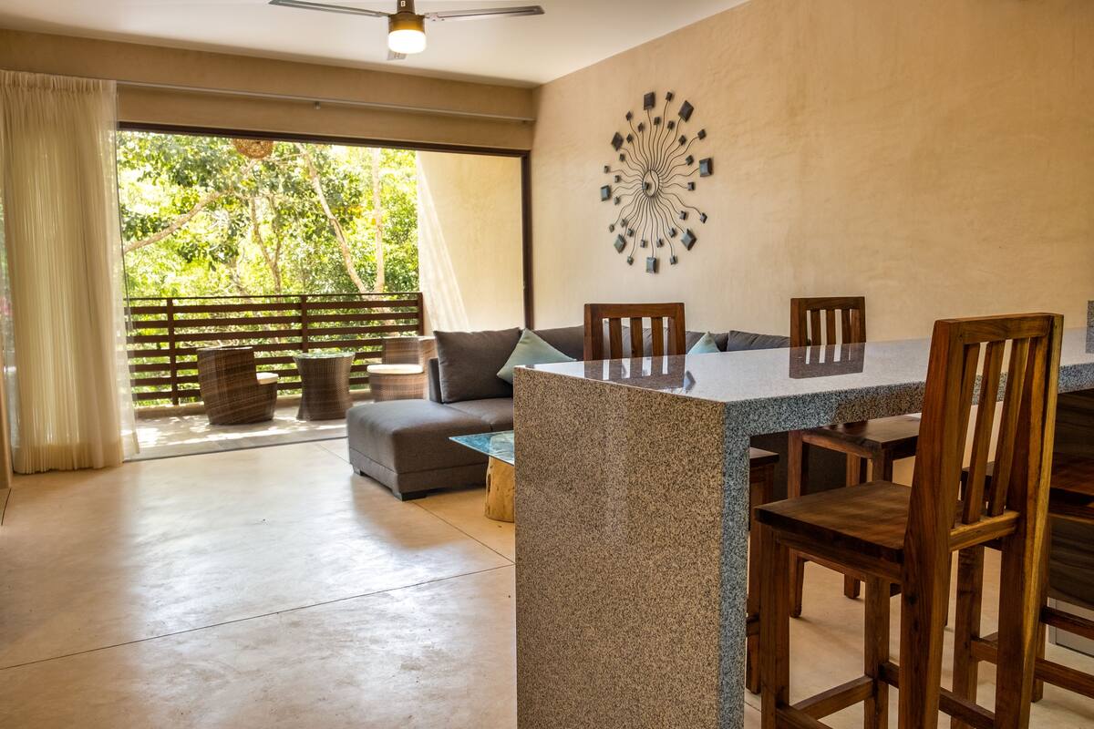 A dining area with a granite table, wooden chairs, a sofa, and a decorative wall piece.