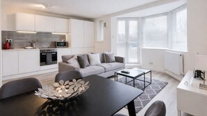 A modern apartment with a kitchen, dining area, and living room. It includes a sofa, a coffee table, and a decorative plant. - Roomspace Apartments -Kew Bridge Court (London)